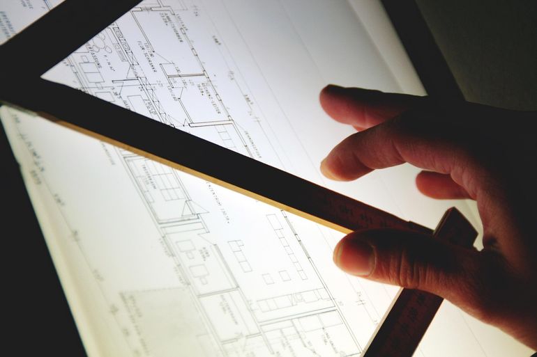 Архитектор работает с чертежом дома на столе с инструментами