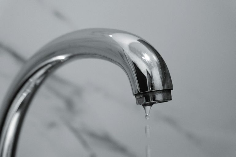 Капля воды срывается с хромированного смесителя в ванной