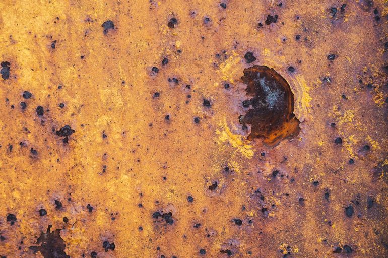 Тёмная шероховатая поверхность с неровным швом и следами коррозии по кромке