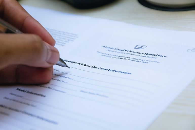 Рука с ручкой подписывает бумажный документ на столе